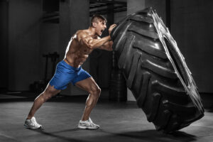 Muscular Guy in Blue Shorts Pushing a huge tire