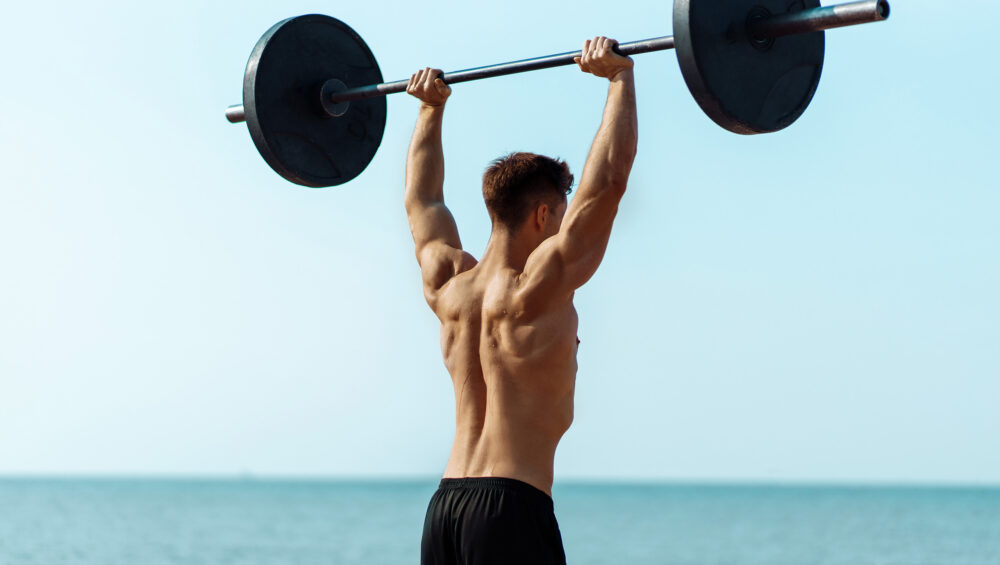 Guy On The Beach Lifting A Dumbell Over Their Head