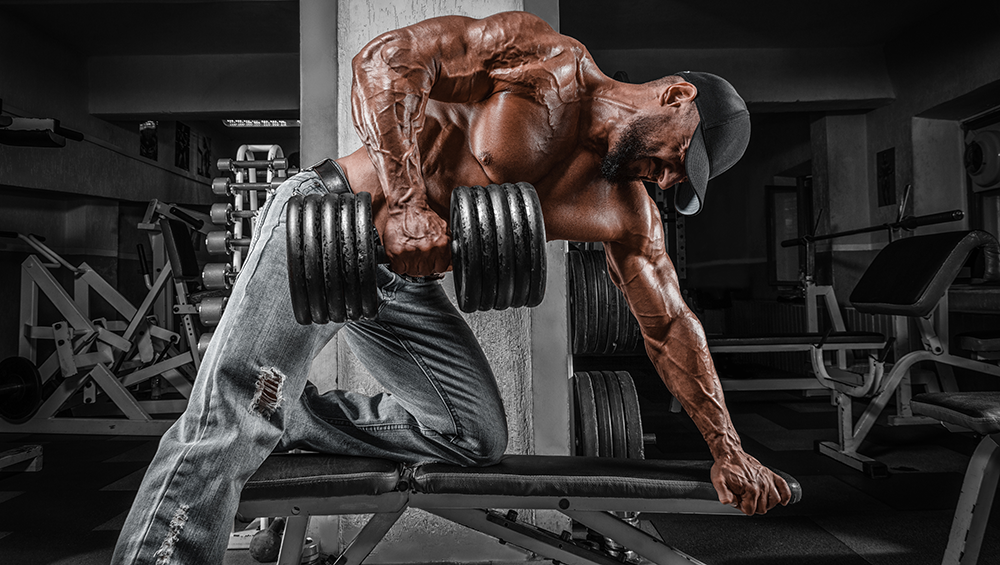 Muscular shirtless guy doing a barbell row on a bench